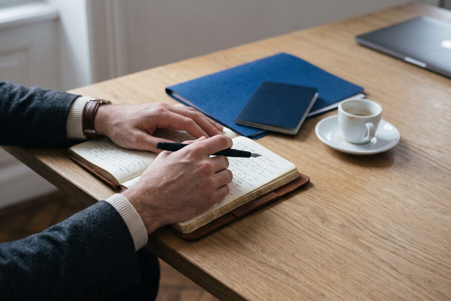 Hands taking notes beside documents on an oak desk